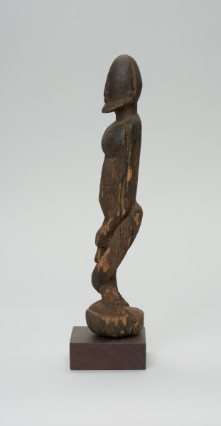 rzeźba - Ujęcie lewego boku. Figura przedstawiająca postać przodka -  mężczyznę ze skrzyżowanymi nogami. Figura antropomorficzna, oddająca cechy dogońskiego kanonu przedstawiania ludzi.