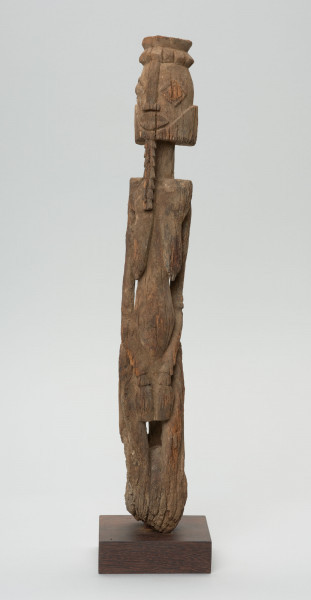 rzeźba - Ujęcie z przodu; Figura - postać kobiety  - przodka, obdarzona została bowiem ozdobną brodą, czyli pewną cechą męską. Głowa i korpus oddzielone od szyi prostymi cięciami. Oczy duże wypukłe, piersi długie, płaskie, nogi zatarte w wyniku używania. Związana z kultem przodków.