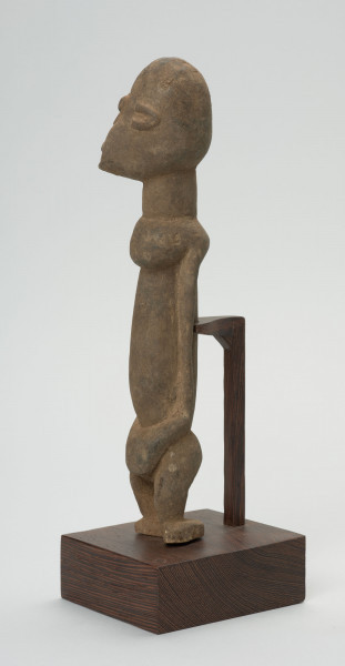 rzeźba - Ujęcie ze skosu z prawej; Figura - postać przodka. Głowa i korpus w stosunku do nóg bardzo duże - co typowe jest dla sztuki dogońskiej. Na uwagę zasługuje przedstawienie twarzy, wykonane nie centralnie, ale z prawej strony. Co nadaje postaci cechy komiczne. I wprowadza do zwykle statycznych wizerunków trochę ruchu.