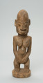 rzeźba - Ujęcie z przodu; Figura - postać kobiety w pozycji stojącej. Sylwetka masywna, przysadzista. Głowa duża, z wyrzeźbionymi uszami. Ręce i piersi wydobyte z bryły głębokimi nacięciami. Dłonie ułożone na łonie. Widoczne stopy. Związana z kultem przodków.