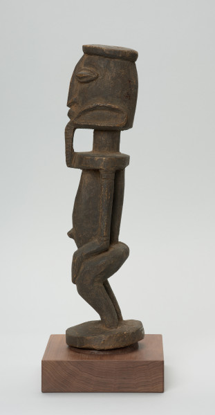 rzeźba - Ujęcie lewego boku. Postać stojąca, z ugiętymi w kolanach nogami. Głowa i tułów wyodrębnione od szyi prosta linią. Oczy, nos, usta wypukłe, broda dekoracyjna sięgająca górnej części tułowia. Ręce przylegające do tułowia, dłonie ułożone na kolanach, brzuch zaokrąglony, z wyraźnie wyodrębnionym pępkiem.