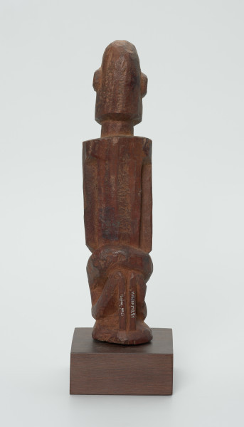 Drewniana figurka mężczyzny z brodą - Ujęcie z tyłu. Drewniana figurka mężczyzny siedzącego na stołku. Kompozycja zgeometryzowana. Na twarzy zaznaczona broda. Głowa bez włosów.