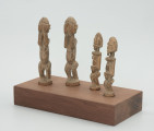 rzeźba - Ujęcie ze skosu z prawej; Zestaw czterech jasnych, drewnianych figurek przedstawiających postacie ludzkie w pozycji stojącej – dwie kobiety i dwóch mężczyzn. Większa para ma zakryte dłońmi oczy. Rysy twarzy – w postaci oczu, strzałkowego nosa, ust i brody – zaznaczono na mniejszych rzeźbach, których ręce przylegają do tułowia, a dłonie oparto o lekko wypukły i wystający brzuch. Wszystkie rzeźby mają krótkie, ugięte w kolanach nogi. Nie zaznaczono im stóp, w ich miejscu wyrzeźbiono okrągłe podstawki. Wszystkie figurki zostały umieszczone przez konserwatora na prostokątnej, drewnianej, ekspozycyjnej podstawie.