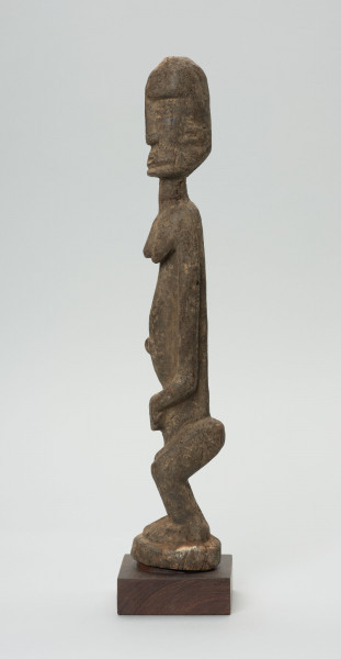 rzeźba - Ujęcie z prawego boku; Figura - postać kobiety w pozycji stojącej. Głowa oddzielona od szyi prostą linią. Okrągłe czoło, nos długi, prosty, strzałkowaty, usta i oczy szerokie. Ręce wydobyte płytkimi nacięciami z bryły korpusu. Dłonie spoczywają na łonie. Nogi ugięte w kolanach. Zaznaczone stopy.