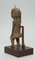 rzeźba - Ujęcie z tyłu z lewej strony. Figura przedstawiająca mężczyznę, o czym świadczy lekko zaznaczony penis. Prawa ręka krótsza od lewej, uniesiona do góry. Ramiona proste, pośladki i uda zaokrąglone. Na głowie wbity kawałek żelaza. Związana z kultem przodków.