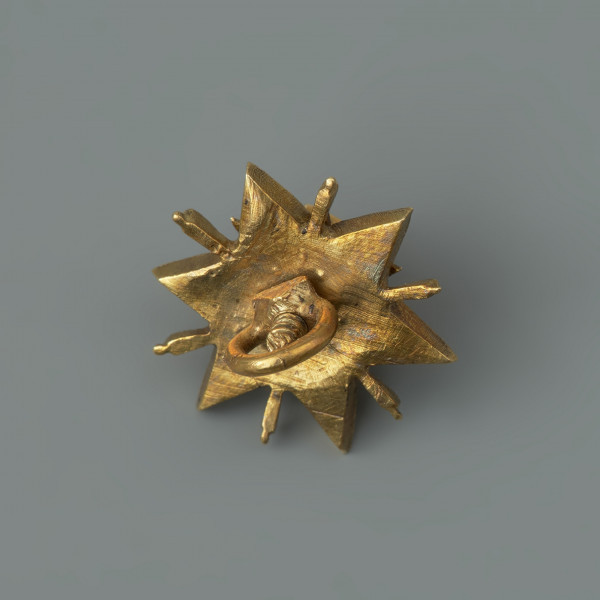 pontalik w kształcie gwiazdki - Ujęcie z tyłu. Podstawa w kształcie sześcioramiennej gwiazdki, kameryzowanej diamentami o szlifie rozetowym. Ramiona gwiazdki rozdzielone wąskimi promieniami pokrytymi białą emalią. W górnej części rozetka z sześciu lancetowatych liści, na niej zwieńczenie w formie kasztu z niezachowanym kamieniem. Poszczególne części połączone śrubą. Na spodzie uszko służące do mocowania klejnotu do stroju.