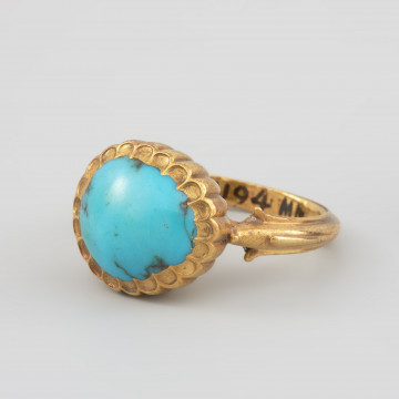 Pierścień z turkusem księcia Franciszka I (1577 - 1620) - Ujęcie z przodu. Pierścień z dużym owalnym turkusem w promieniście puklowanej pełnej oprawie. Szyna o profilowanych brzegach, rozszerzająca się w stronę oprawy. Końce szyny ujmujące oprawę kamienia zakomponowane zostały z motywów roślinnych, zbliżonych kształtem do paszczy fantastycznych zwierząt.