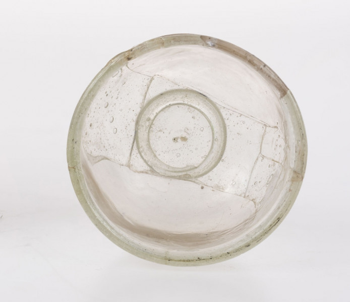 Naczynie szklane w formie pucharka na pierścieniowatej stopce. Stopka dolepiana ze śladem przylepca. Wylew wychylony o zaokrąglonej krawędzi. Pod wylewem znajduje się pozioma nitka obiegająca korpus 1,5 raza. Brzusiec zaokrąglony przechodzący w płaską część przydenną. Naczynie określane jako 