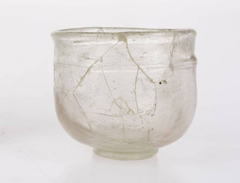 Naczynie szklane w formie pucharka na pierścieniowatej stopce. Stopka dolepiana ze śladem przylepca. Wylew wychylony o zaokrąglonej krawędzi. Pod wylewem znajduje się pozioma nitka obiegająca korpus 1,5 raza. Brzusiec zaokrąglony przechodzący w płaską część przydenną. Naczynie określane jako 