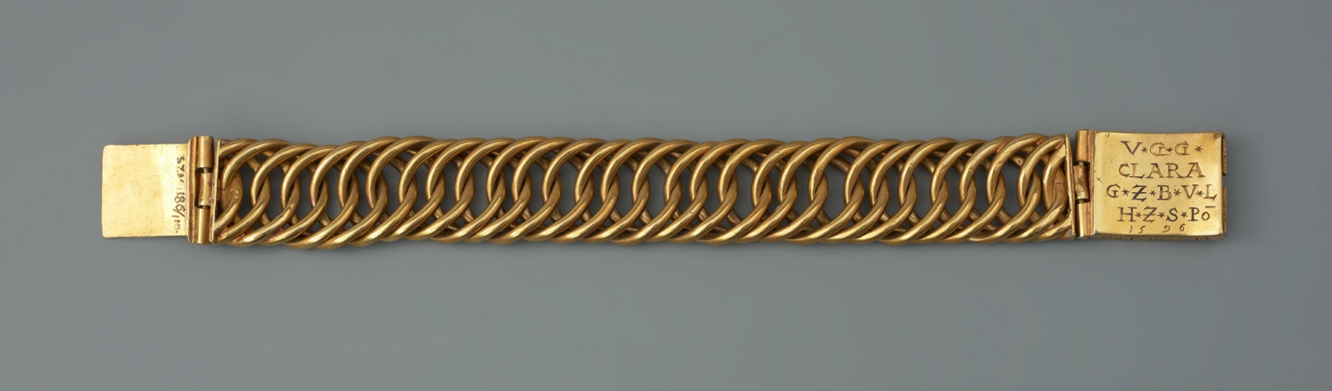 Bransoleta z sarkofagu księcia Franciszka I (1577 - 1620) - Ujęcie z tyłu. Bransoleta wykonana ze skręconych, przenikających się ogniw, w tzw. splocie pancerzowym. Na prostokątnych zapinkach dziewięciopolowy herb Księstwa Pomorskiego trzymany przez dzikich mężów, pierwotnie emaliowany. Na spodzie klamry ryta inskrypcja, pierwotnie emaliowana: V.G.G. / CLARA / G.Z.B.V.L. / H.Z.S.Pō /15.96. Na bocznych ściankach wykonana w tej samej technice inskrypcja: V.G.G. FRANTZ / H.Z.S.Pom.