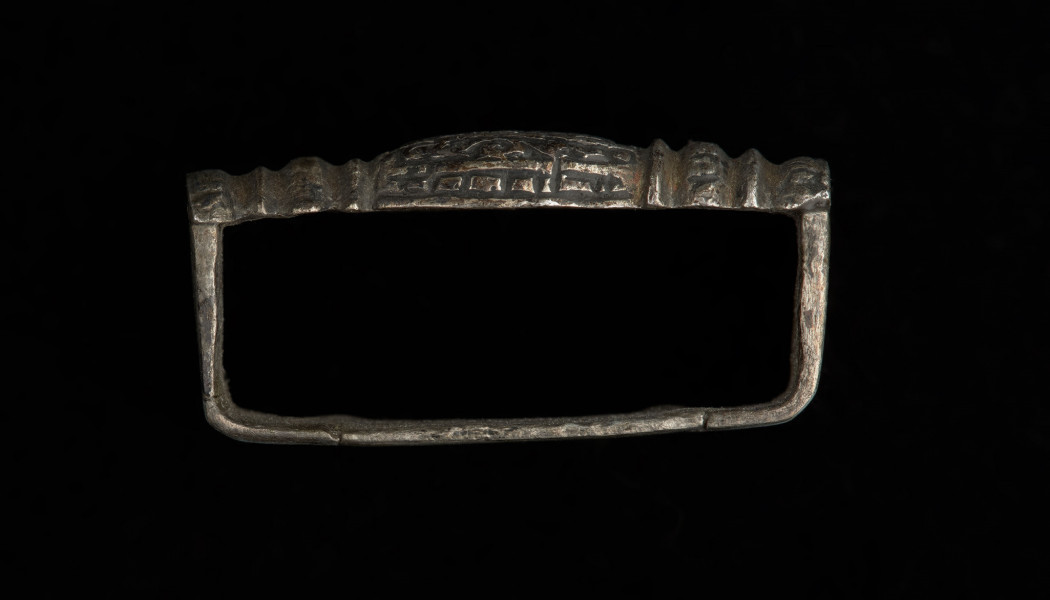 Szlufka do pendentu księcia Kazimierza VI/IX (1557-1605) - Ujęcie z boku z góry. Prostokątna szlufka wykonana z gładkiej, srebrnej taśmy, z ozdobnie opracowaną częścią przednią w formie tralki, pokrytą grawerowaną i niellowaną dekoracją.