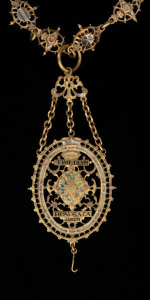 odznaka honorowa elektora saskiego Jana Jerzego I - Ujęcie odznaki z tyłu z zawieszką. Odznaka o owalnym kształcie, ażurowa, emaliowana. Jej głównym elementem jest czarny dwugłowy orzeł w koronie cesarskiej. Na awersie, na piersi orła herb Saksonii Elektorskiej. W owalnej ramce, otoczonej rucianym wieńcem inskrypcja: SVB. VMBRA. ALARUM. TUARUM.1.6.11. Na rewersie na tułowiu orła wieniec z kwiatkami trzymany przez dwie dłonie. W otoku napis: PRVS. MOR. QVAM. FIDEM. FALLIERE. U dołu szczątkowo zachowana perła. Odznaka przy pomocy trzech łańcuszków połączona jest z ażurową plakietką z uszkiem. Łańcuch składa się z dziesięciu owalnych ogniw z emaliowanymi herbami prowincji saskich (różnymi po obu stronach). Między nimi ogniwa z motywem dłoni trzymających zielony wieniec z białymi kwiatkami, a także gładkie okrągłe ogniwa i ogniwa o fakturze plecionki. Na emaliowanej, kolistej zapince motyw dwugłowego orła z herbem Saksonii Elektorskiej.