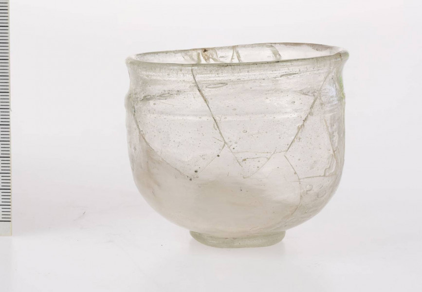 Naczynie szklane w formie pucharka na pierścieniowatej stopce. Stopka dolepiana ze śladem przylepca. Wylew wychylony o zaokrąglonej krawędzi. Pod wylewem znajduje się pozioma nitka obiegająca korpus 1,5 raza. Brzusiec zaokrąglony przechodzący w płaską część przydenną. Naczynie określane jako 