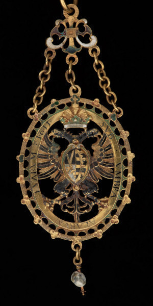 odznaka honorowa elektora saskiego Christiana II - Ujęcie medalu z tyłu. Odznaka o owalnym kształcie, ażurowa, emaliowana. Na awersie pośrodku tarcza migdałowa z elektorskim herbem dzielonym. W otaczającym ją ornamencie na dwóch tabliczkach dewiza: A DEO / PRO IMPERIO. Nad inskrypcją oko opatrzności. Na rewersie w środkowym polu motyw słońca w otoczeniu sześciu gwiazd. Na tabliczkach inskrypcja: „TIME DEUM / HONORA CAESAREM”. U dołu zawieszenia sztyft będący pozostałością po perle. Odznaka przy pomocy trzech łańcuszków połączona jest z ażurową plakietką z uszkiem. Łańcuch składa się z 30 ozdobnych, ażurowych, emaliowanych ogniw, połączonych kółkami ze złotego drutu. Na połowie z nich ukazano emaliowane herby 15 prowincji saskich. Na pozostałych 15 przedstawiono serce z literą C i kapeluszem elektorskim, trzymane w dwóch dłoniach. Na kolistej zapince emaliowany herb elektorskiej Saksonii.