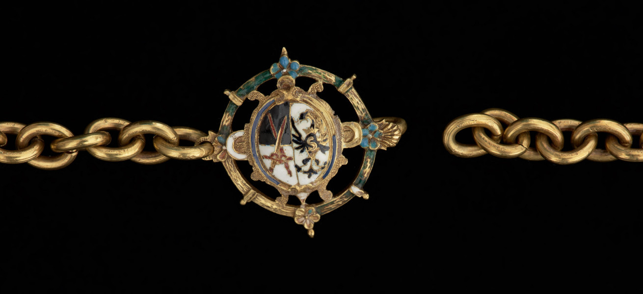 wisior - medalion z portretami elektora saskiego Jana Jerzego I i jego żony - Ujęcie zapięcia. Owalny, dwustronny medalion pierwotnie z portretami malowanymi na blasze miedzianej, umieszczonymi pod kaboszonami z kryształu górskiego. Ażurowa, emaliowana oprawa, zdobiona jest diamentami o szlifie tablicowym, w kwadratowych kasztach. U dołu trzy sztyfty po brakujących podwieszonych perłach. Medalion połączony trzema łańcuszkami z ażurową plakietką z uszkiem, zdobioną emalią i pojedynczym diamentem po obu stronach. Łańcuch z gładkich, owalnych ogniw zakończony okrągłą, ażurową zapinką z herbami Saksonii i Brandenburgii.