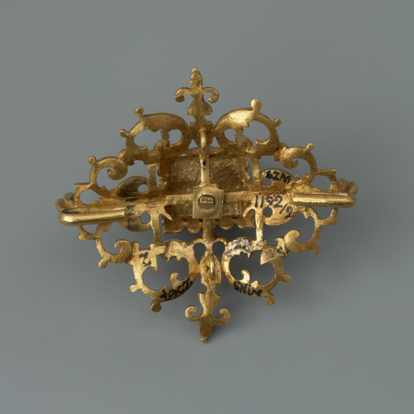 rozeta z kołpaka księcia Filipa II (1573-1618) - Ujęcie z tyłu. Klejnot zbudowany z dwóch skręconych ze sobą śrubą części: ażurowego stelaża o romboidalnym kształcie i osadzonej na nim wysokiej, kasetowej oprawy, ujmującej diament o szlifie tablicowym. Stelaż i ścianki kasztu pokryte barwną emalią, korpusową, a także żłobkową, z wzorami rezerwowanymi w złocie. Rozety mają na spodniej stronie, w narożach, haczyki umożliwiające spinanie ich w łańcuch, a także uszka pozwalające na ich mocowanie do stroju.