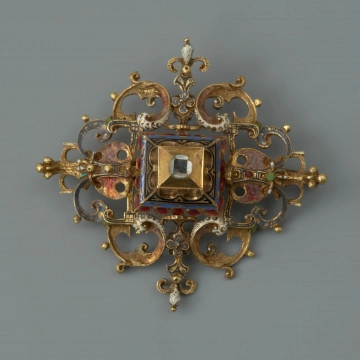 rozeta z kołpaka księcia Filipa II (1573-1618) - Ujęcie z przodu. Klejnot zbudowany z dwóch skręconych śrubą części: ażurowego stelaża o romboidalnym kształcie i osadzonej na nim wysokiej, kasetowej oprawy, ujmującej diament o szlifie tablicowym. Stelaż i ścianki kasztu pokryte są barwną emalią, korpusową, a także żłobkową, z wzorami rezerwowanymi w złocie. Rozety mają na spodniej stronie, w narożach, haczyki umożliwiające spinanie ich w łańcuch, a także uszka pozwalające na ich mocowanie do stroju.