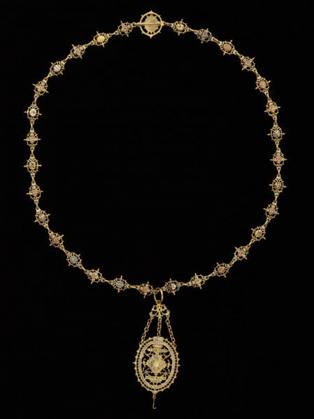 odznaka honorowa elektora saskiego Jana Jerzego I - Ujęcie odznaki z tyłu z łańcuchem. Odznaka o owalnym kształcie, ażurowa, emaliowana. Jej głównym elementem jest czarny dwugłowy orzeł w koronie cesarskiej. Na awersie, na piersi orła herb Saksonii Elektorskiej. W owalnej ramce, otoczonej rucianym wieńcem inskrypcja: SVB. VMBRA. ALARUM. TUARUM.1.6.11. Na rewersie na tułowiu orła wieniec z kwiatkami trzymany przez dwie dłonie. W otoku napis: PRVS. MOR. QVAM. FIDEM. FALLIERE. U dołu szczątkowo zachowana perła. Odznaka przy pomocy trzech łańcuszków połączona jest z ażurową plakietką z uszkiem. Łańcuch składa się z dziesięciu owalnych ogniw z emaliowanymi herbami prowincji saskich (różnymi po obu stronach). Między nimi ogniwa z motywem dłoni trzymających zielony wieniec z białymi kwiatkami, a także gładkie okrągłe ogniwa i ogniwa o fakturze plecionki. Na emaliowanej, kolistej zapince motyw dwugłowego orła z herbem Saksonii Elektorskiej.