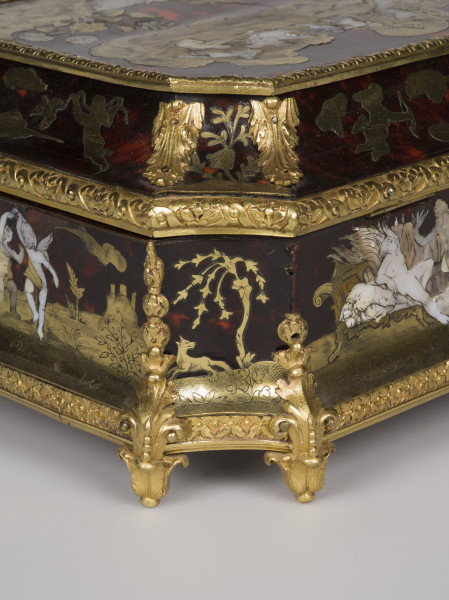 zbliżenie na zdobienie na lewym tylnym rogu - motyw roślinny, widok na fragment wieka i narożnik. Na pierwszym planie wilk z drzewem, po lewej tańczące amorki po prawej kobieta leżąca na łożu, krawędzie ścianek i wieka pokryte dekoracjami z brązu w postaci palmet i ornamentu kwiatowego, nóżki w postaci rozety liści.