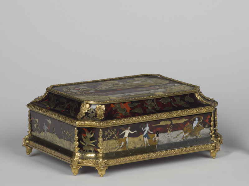 ujęcie 3/4, widok z boku od góry, szkatułka z prostopadłościenna z wklęsłymi półkoliście narożnikami. Czarne ściany pokryte inkrustacją z mosiądzu, masy perłowej i szylkretu o motywach figuralnych i roślinnych. Wszystkie krawędzie szkatułki pokryte dekoracjami z brązu w postaci palmet i ornamentu kwiatowego. Nóżki szkatułki w postaci rozety liści. Na ściankach bocznych po prawej stronie dekoracja przedstawiająca Porwanie Europy, postać kobiety i mężczyzny obok kobieta jadąca na byku po lewej na ściance bocznej amorek od tyłu, pośrodku dekoracja roślinna i zwierzę.