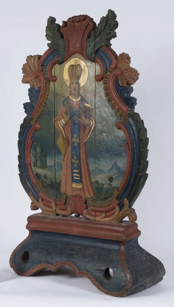 E/16801/ML - Feretron drewniany polichromowany. Z kręgu sztuki prawosławnej. W obramieniu trójlistnym ze stylizowanymi liśćmi akantu, przedstawia Matkę Bożą Chełmską i Św. Mikołaja. 
Madonna z Dzieciątkiem: w niebieskiej szacie ze złotym wykończeniem przy szyi, czerwonym płaszczu, złotej koronie. Na prawym ramieniu trzyma Dzieciątko, w biało-szarej szacie i złotej koronie. Wzrok postaci skierowane ku sobie. Wokół głów – złote nimby. Karnacja cielisto-brązowa. Tło ciemnobrązowe. Po obu stronach głów postaci litery.
Św. Mikołaj: postać stojąca w czerwono-niebieskiej szacie ze złotymi lamowaniami. W lewej, zgiętej w łokciu ręce – księga, brązowa ze złotymi kartami. Prawa ręka zgięta i uniesiona w geście błogosławieństwa; pod nią torba. Na szyi – łańcuch z krzyżem. Na głowie biskupia korona, a wokół niej złoty nimb. Po obu stronach postaci, na wysokości ramion, napisy w j. greckim. W tle pejzaż ze wzniesieniem i roślinnością, a po lewej stronie przedstawienia – cerkiew. 
Kolory obramienia feretronu: ceglasty, czerwony, granatowy, ciemnozielony. 

Konserwacja: 1999-2000