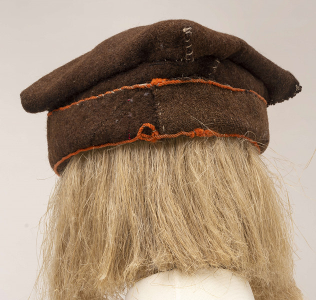 Czapka męska rogatywka szyta ręcznie z samodziałowego sukna w kolorze brązowym. Jeden pas stanowi otok., drugi tej samej szerokości jest wywinięty na wierzch i obszyty na dolnej i górnej krawędzi pomarańczowym wełnianym sznureczkiem. Górna cześć czapki wykonana z kwadratowego płata z wywiniętymi narożnikami, które po zszyciu i przyszyciu do otoka tworzą płaskie kwadratowe denko, o wym. 20 x 20 cm. Noszona do sukmany.