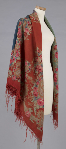 E/7995/ML - Chusta z cienkiej wełny. Powierzchnia podzielona bukietami kwiatów (róże i niezapominajki) na 4 pola w kolorach: czerwonym, zielonym, fioletowym i szafirowym. W każdym narożniku duży bukiet kwiatów oraz tzw. turecki motyw w formie łezki. Bordiura w kolorze czerwonym, na niej wieniec z większych i mniejszych bukietów. Noszona na ramionach. 