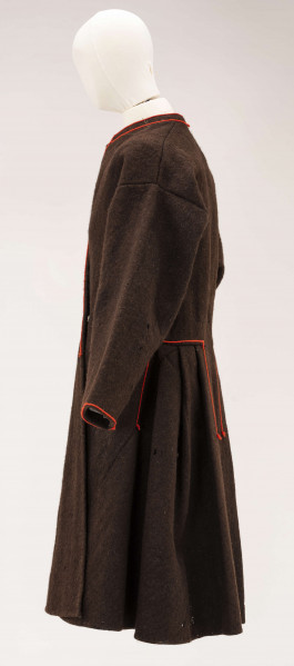 Sukmana męska, odświętna, szyta ręcznie z samodziałowego, folowanego sukna w kolorze ciemnobrązowym. Uszyta z 7 części: rękawy z jednego kawałka, zwężone ku dołowi, przody, plecy i dwa kliny uzupełniające fałdowanie poniżej talii z tyłu. Przody gładkie rozszerzone lekko ku dołowi, ozdobione przy zapięciu pomarańczowym sznureczkiem, który ozdabia również wycięcie wokół szyi. Tył sukmany, poniżej talii, fałdowany – po bokach symetrycznie ułożone po 3 fałdki o szer. 4 cm. W bokach, poniżej talii, rozcięcia tworzące ślepe kieszenie. Przy kieszeniach i wokół fałdowania obszycia proste z pomarańczowego sznurka.