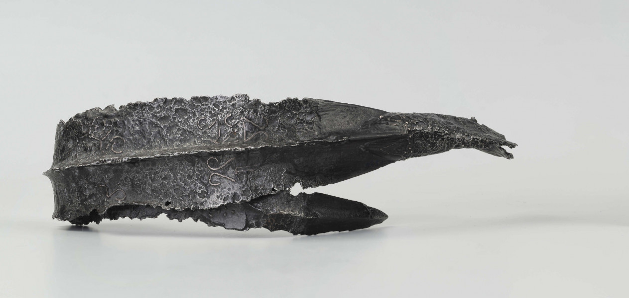 Żelazny grot broni drzewcowej zdobiony wyjątkową, srebrną inkrustacją jest częścią uzbrojenia włożonego do grobu ciałopalnego wojownika z początku III w. n.e. 
Grób przedstawiciela ludności kultury przeworskiej został odkryty przypadkowo w 1959 roku. 
Oprócz trzech grotów, pochówkowi wojownika towarzyszyły: żelazne umbo, dwie ostrogi, tok brązowy (prawdopodobnie okucie drzewca oszczepu) a także żelazny miecz z miedziana inkrustacją wyobrażającą rzymskich bogów. Pochowany na terenie obecnej wsi Podlodów wojownik należał do elity wojskowej przedstawicieli kultury przeworskiej. Liść grotu jest smukły i długi, a u podstawy cylindrycznej i krótkiej tulejki znajduje się żeberko. Na obydwu częściach grotu znajdują się zdobienia inkrustowane srebrem - znaki o znaczeniu symbolicznym: trójkąty sferyczne, punkty, podwójne widełki. Przypominają one symbole religijne (ewentualnie znaki magiczne lub własnościowe) - tamgi. Niektórzy badacze zakładają, że mogły one zostać przejęte przez Sarmatów. 
Wymiary dodatkowe: szer. 4,0 cm 