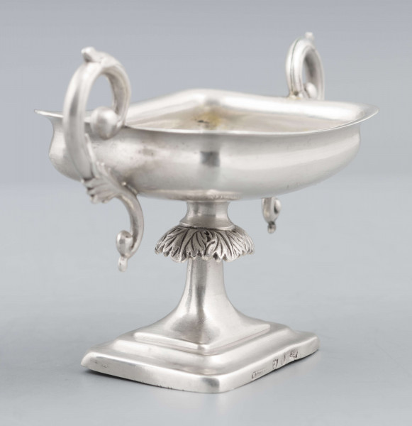 S/Mt/57/ML - Stopa prostokątna, wysklepiona, przechodząca w trzon z owalnym kapturkiem sztancowanym we wzór akantu. Czarka prostokatna o zaokrąglonych narożach i wywinietym brzegu, z dwoma uchami na krótszych bokach. Ucha wolutowe zdobione listkami. 