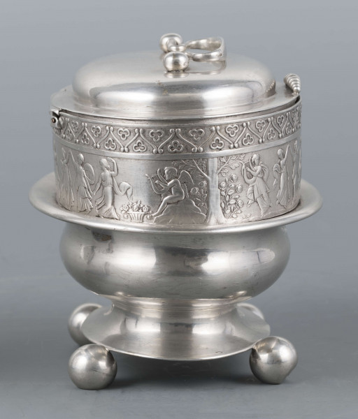 S/Mt/363/ML - Cukiernica owalnana niskiej stopie z czterema kulistymi nóżkami, z pokrywką w formie wieczka.
Podzielona na dwie części : 
- część dolna lekko wybrzuszona, o gładkiej powierzchni, kończy się w połowie wysokości wywiniętym kołnierzem; - część górna prosta uformowana jest z moletowanej taśmy, na której powtarza się trzykrotnie scenka antyczna: po rawej siedzący pod drzewem amorek gra na lirze, po lewej stoi grająca na lirze kobieta, pomiędzy nimi tańczą trzy inne.Górną krzwędź obiega pas stylizowanych neogotyckich trójliści.