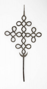 Krzyż o ramionach wykonanych z płaskich prętów żelaznych, powyginanych w ten sposób, że tworzą małe krzyżyki. W dolnej części krzyża przynitowany półksiężyc. Dolny koniec środkowego ramienia w postaci obłego pręta.