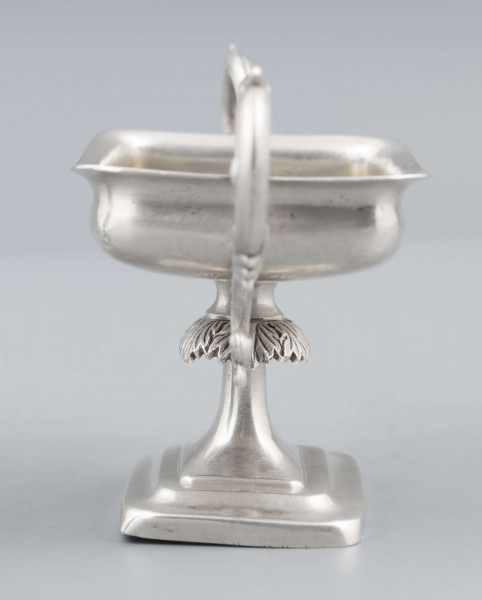 S/Mt/57/ML - Stopa prostokątna, wysklepiona, przechodząca w trzon z owalnym kapturkiem sztancowanym we wzór akantu. Czarka prostokatna o zaokrąglonych narożach i wywinietym brzegu, z dwoma uchami na krótszych bokach. Ucha wolutowe zdobione listkami. 