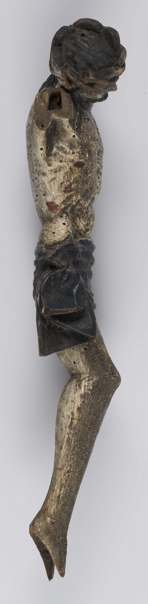 E/15978/ML - Rzeźba drewniana przedstawiająca Chrystusa Ukrzyżowanego, bez rąk. Wydłużony z wystającą klatka piersiową i linearnie zaznaczonymi żebrami, osłonięty pofałdowanym perizonium ozdobionym dekoracją snycerską w postaci ukośnych kresek. Głowa mocno przechylona , wsparta na prawym ramieniu. Twarz wydłużona o oczach osadzonych blisko siebie, nos prosty, usta wąskie okolona brodą. Na głowie korona cierniowa, włosy długie zaznaczone ukośnymi rzeźbionymi kreskami. Głowa, włosy, perizonium pokryte czarną olejną farbą, korpus biały.