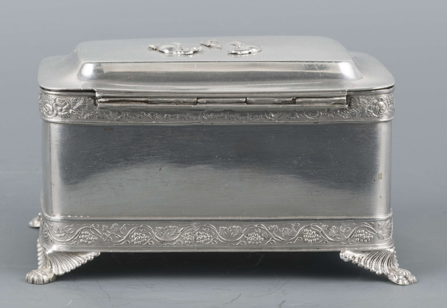 S/Mt/354/ML - Cukiernica prostokątna o lekko zaokrąglonych narożach, na czterech nóżkach w formie uskrzydlonych lwich łap, z profilowanym wieczkiem. Brzegi obwiedzione moletowaną taśmą: u dołu z motywem winnej łozy, u góry - wici różanej.Szyld zamka zdobi plakieta z girandą róż, druga - na wieczku - jest uszkodzona a przez to nieczytelna.
Na dnie sygnatury kursywa we wklesłych owalnych ramkach:
- K.Rotkiel
- w lublinie
Przedzielone okrągłą puncą z próbą 