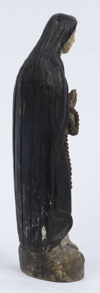 E/6363/ML - Rzeźba z drewna lipowego, polichromowana farbą olejną. Zakomponowana w jednym kawałku drewna na postumencie o formie owalnej z płaskorzeźbionym motywem dwóch skrzyżowanych gałęzi. Postać stojąca przedstawia Matkę Boską Różańcową. Twarz owalna, głęboko osadzone oczy, prosty i szeroki nos, małe pełne usta. Ręce zgięte w łokciach: duże dłonie złożone do modlitwy. Na przedramieniu prawej ręki brązowy różaniec o płaskich paciorkach, zakończony dużym krzyżem. Postać odziana w białą prostą suknię, gładko wykończoną pod szyją i przewiązaną granatową szarfą. Na głowie granatowa szata spełniająca jednocześnie rolę peleryny spływającej z ramion ku dołowi i spowijającej całą postać.