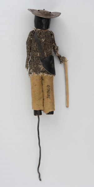 Figurka z szopki - blacharz. Kadłub drewniany na drucie. Twarz lekko ciosana. Rysy twarzy zaznaczony farbą. Blaszany kapelusz, szaro-czarna bluza, rude spodnie. Przez ramię przewieszona torba skórzana na pasku. Na piersi przymocowane narzędzia kuchenne z blachy. W prawym ręku drewniany kij.