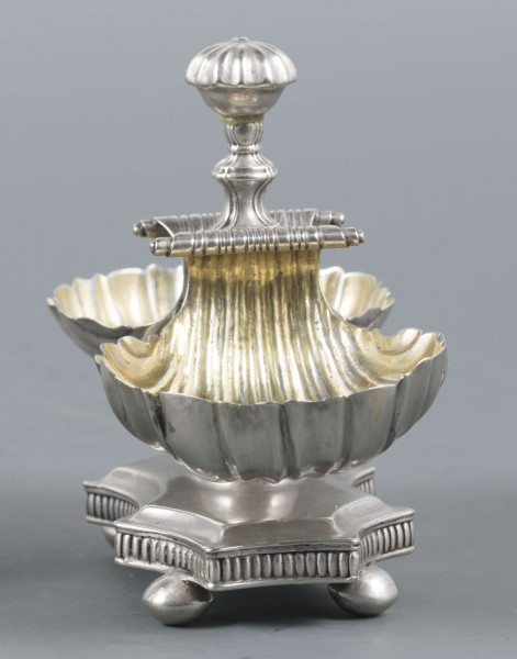 S/Mt/494/ML - Solniczka składa się z dwóch czarek w formie muszli połączonych z pionowym, profilowanym uchwytem o zwieńczniu w formie makówki ustawionym na wydłużonej ośmiobocznej podstawie o wklęsłych bokach. Krawędź podstawy fasetowana, boki karbowane, cztery nóżki w kształcie spłaszczonych kulek. Wnetrze muszli złocone.
Na dnie podstawy sygnatura kursywą w owalnych ramkach:
- J.Gałecki
- w Lublinie
- punca owalna z przedstawieniem dłoni (sygnatura pomocnicza)
- wężyk probierczy
- znak probierni warszawskiej z próbą 