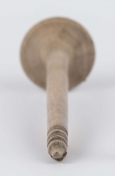 E/8019/ML - Przęślica krężołkowa z drewna brzozowego składa się z cienkiej deski – przysiadki, w której przy jednym końcu osadzona jest pionowa beleczka zw. piórem, z nasadzonym od góry ruchomym krężlem w kształcie wydłużonego stożka. Deseczka przysiadki o kształcie prostokątnym lekko zwężającym, od ok. połowy swej długości w kierunku pióra, i zakończonym głową zwierzęcą – psa. Pióro i krężel ozdobnie toczone. Krężel ma kształt stożka z rozszerzoną podstawą, w której znajduje się stożkowaty otwór, do osadzenia krężla na piórze. Dekoracja snycerska ryta znajduje się na zwężającej części przysiadki. Część zdobiona oddzielona małym stopniem. Grubość przysiadki w części zdobionej 2x większa od pozostałej części. Dekoracja snycerska tworzy ornament roślinny w postaci trzech ulistnionych drobno gałązek. Na zakończeniu ornamentu znajdują się ryte liście oraz inicjały „K.F.”. Głowa psa zdobiona drobnymi nacięcia. Zakończenie przysiadki wycięte faliście.