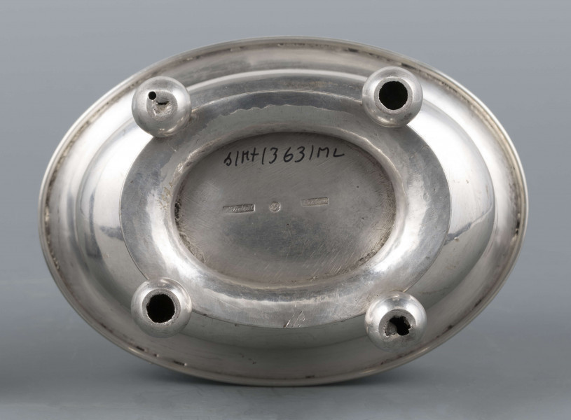 S/Mt/363/ML - Cukiernica owalnana niskiej stopie z czterema kulistymi nóżkami, z pokrywką w formie wieczka.
Podzielona na dwie części : 
- część dolna lekko wybrzuszona, o gładkiej powierzchni, kończy się w połowie wysokości wywiniętym kołnierzem; - część górna prosta uformowana jest z moletowanej taśmy, na której powtarza się trzykrotnie scenka antyczna: po rawej siedzący pod drzewem amorek gra na lirze, po lewej stoi grająca na lirze kobieta, pomiędzy nimi tańczą trzy inne.Górną krzwędź obiega pas stylizowanych neogotyckich trójliści.