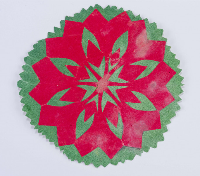 Wycinanka naklejona z zielonego i czerwonego papieru. Tło zielone o kształcie 8boku. Z czerwonego papieru wycięta 16ramienna o ramionach ażurowanych w serduszka i gwiazdkę.

