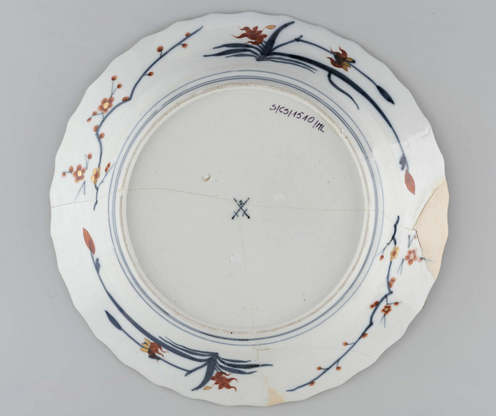 Półmisek okrągły o brzegu falistym. Na kołnierzu szeroka bordiura typu lambrekinowego z dodanymi motywami kwiatowymi, pośrodku dna gałązka kwiatowa, wokół regularnie rozmieszczone mniejsze. Dekoracja dwubarwna: partie kobaltowe malowane pod szkliwem, kwiaty malowane czerwienią naszkliwnie, całość o rysunku podkreślonym złoceniem. Na odwrocie kołnierza malowane gałęzie śliwy i irysów.
 