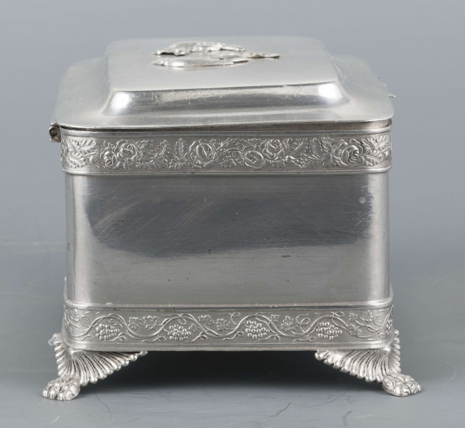 S/Mt/354/ML - Cukiernica prostokątna o lekko zaokrąglonych narożach, na czterech nóżkach w formie uskrzydlonych lwich łap, z profilowanym wieczkiem. Brzegi obwiedzione moletowaną taśmą: u dołu z motywem winnej łozy, u góry - wici różanej.Szyld zamka zdobi plakieta z girandą róż, druga - na wieczku - jest uszkodzona a przez to nieczytelna.
Na dnie sygnatury kursywa we wklesłych owalnych ramkach:
- K.Rotkiel
- w lublinie
Przedzielone okrągłą puncą z próbą 