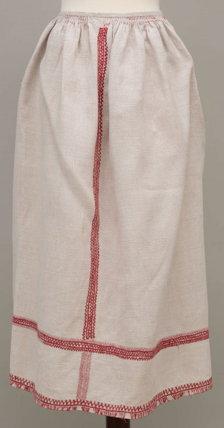 Fartuszek lniany zdobiony pośrodku, po bokach i na dole czerwonym haftem, przymarszczony w pasie, wiązany na troczki.