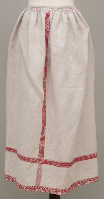Fartuszek lniany zdobiony pośrodku, po bokach i na dole czerwonym haftem, przymarszczony w pasie, wiązany na troczki.