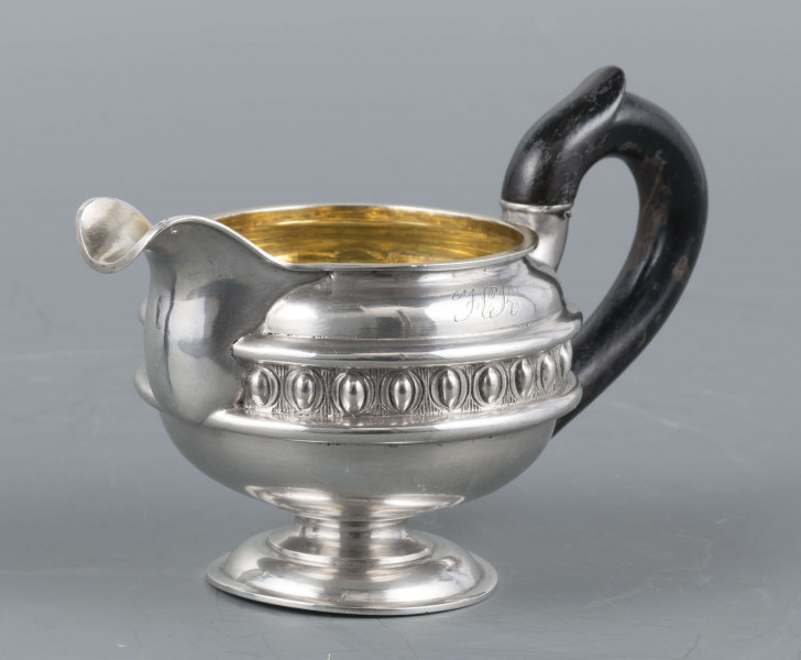 S/Mt/545/ML - Brzusiec w formie spłaszczonej kuli, pośrodku zdobiony repusowanym pasem kimationu obwiedzionego dwoma półwałkami, brzeg górny z okrągłym rantem, wylew wywinięty, zaokrąglony. Wnętrze złocone. Stopa okrągła profilowana, ucho drewniane malowane na czarno, osadzone w dwóch tulejkach . Na brzuscu pod górną krawędzią grawerowany ozdobny monogram 