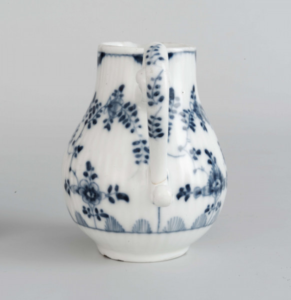 Dzbanek gruszkowaty na niskiej pierścieniowatej podstawie, ucho wolutowe, wylew trókątny, powierzchnia drobno kanelowana. Malowany podszkliwnie błękitem kobaltowym we wzór suchych kwiatów (kocanka), poniżej brzegu górnego na zewnatrz i wewnątrz malowana cienka obwódka, na dnie brzegu uszka gałązka. 
