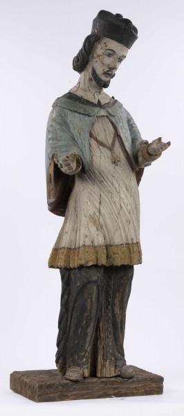 E/8422/ML - Rzeźba drewniana, pełna, polichromowana, przedstawiająca św. Jana Nepomucena. Zakomponowana frontalnie, z rękoma zgiętymi w łokciu i lekko rozłożonymi. Twarz owalna, pomalowana białą farbą. Małą broda i krótkie czarne wąsy. Nos krótki, prosty. Oczy owalne podkreślone czarnym konturem. Brwi łukowate, wąskie, czarne. Włosy czarne, ułożone w pukle. Na głowie czarny biret. Długa czarna sutanna, biała komża ozdobiona u dołu złotą koronką. Na piersiach krzyż, zawieszony na łańcuchu. Na komżę narzucona jasnoniebieska peleryna. Stopy lekko rozstawione. Obuty w sandały o jednym pasku. 

Konserwacja: 1990 r.