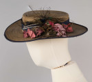 E/560/ML - Kapelusz męski, z cienkiej trzcinki zszywanej nicią. Rondo obszyte niebieską tasiemką, opasane również niebieską (ciemnoniebieską/jasnogranatową) jedwabną wstążką. Kapelusz ozdobiony jest sztucznymi kwiatami białymi i jasnoróżowymi oraz pawimi piórami. Pióra przypiete są metalowo-plastikową broszką.