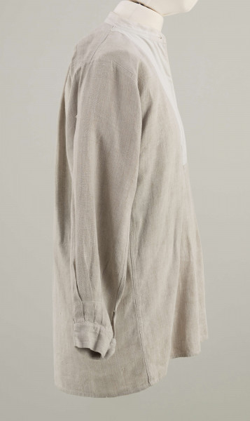 E/9858/ML - Koszula męska z lnianego samodziałowego płótna tkanego splotem prostym, szyta na maszynie. Krój z karczkiem. Wycięcie koło szyi wykończone stójką z białego płótna zapinana na jeden guziczek. Rozcięcie na przodzie o dł. 26 cm zapinane na dwa guziczki, wykończone fałdem o szer. 4,5 cm. Gors naszyty jest cienkim białym płótnem. Rękawy długie, krojone, razem z włokami dołem wzbogacone ośmioma zakładkami ujęte w mankiet o dł. 24 cm szer. 4 cm zapinany na guziczek.